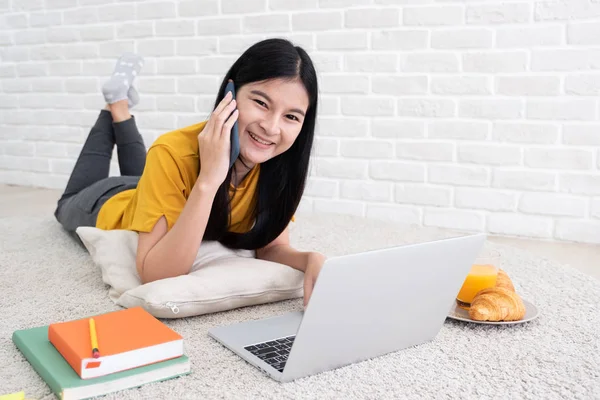 亚洲女性在手机上交谈 并使用笔记本电脑在家工作 女人躺在墙上的地毯上 工作在线生活方式 — 图库照片