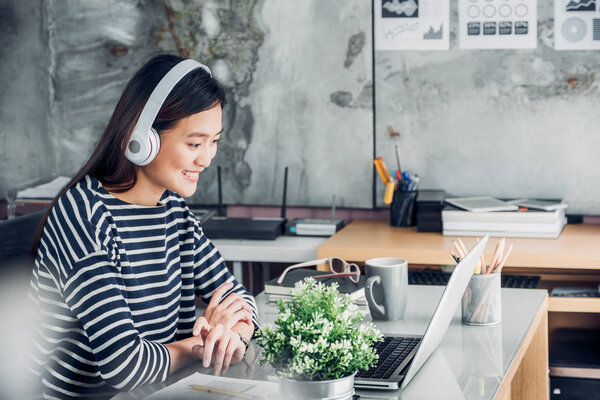 Young asian casual businesswoman arm on desk rest pose with laptop computer and listening music via headphone and think about work ,work at home with relax feeling concept