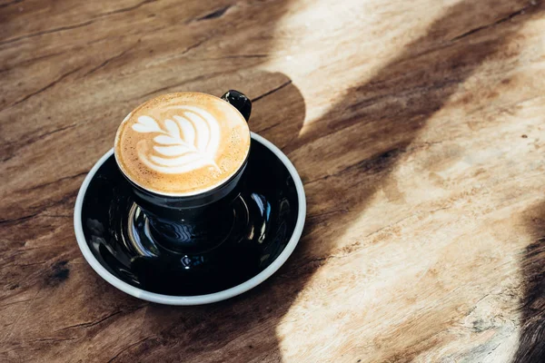 Sıcak siyah kahve fincanı ağaç kalp şekli latte sanat süt köpüğü kafe Restoran, keskin gölge güneş ışığı ile pencere yakınındaki ahşap masa üzerinde ile kapatın. Boş zaman lifestyle.food ve içecek