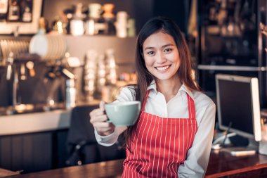 sıcak kahve fincanı tutarak ve mutlu duygu, Cafe restoran hizmet anlayışı, yüzü gülen tarih seçici odak olan sayaç bar gülümseyen Asyalı kadın barista aşınma kırmızı önlük