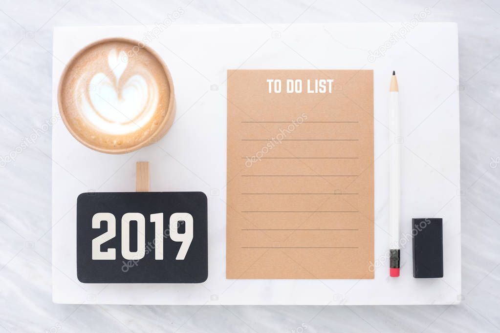2019 to do list on brown recycle paper with pencil,clip blackboard,pencil,eraser and coffee cup on white and grey marble table.mock up for adding text,new year resolution concept