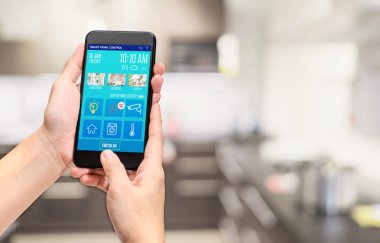 El telefon tutarak akıllı ev kontrol mobil app kullanmak bulanıklık bokeh mutfak arka plan, akıllı yaşam kavramı, dijital yaşam tarzı