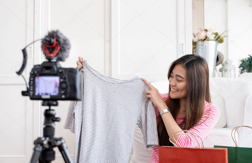 Asian young female blogger recording vlog video with review cloths T-shirt at home online influencer on social media concept.live streaming viral 