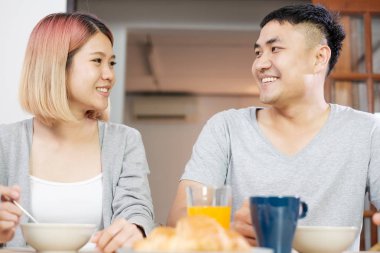 Pijamalı mutlu Asyalı çift sabahları mutfaktaki masada oturup mısır gevreği yiyorlar.