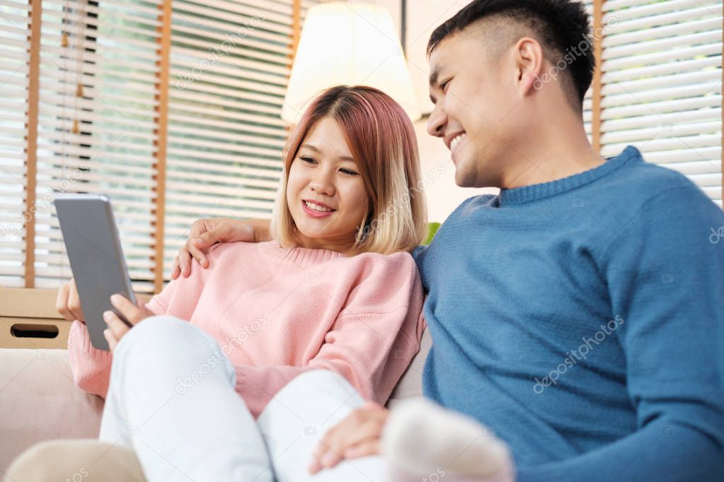 Asian couple watching video live on tablet on sofa in living room at home.lover spending time together
