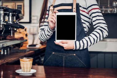 Asyalı kadın barista aşınma jean önlük gülümseme duygu, Cafe restoran hizmet kavramı, yukarıya aygıt ekran metni küçük business.mock sahibi olan sayaç bar müşteri için boş ekran tablet holding