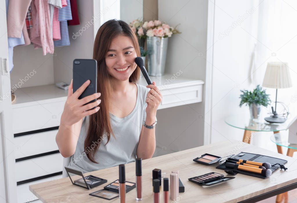 Asian young female blogger recording vlog video use mobile with makeup cosmetic at home online influencer on social media concept.live streaming viral 