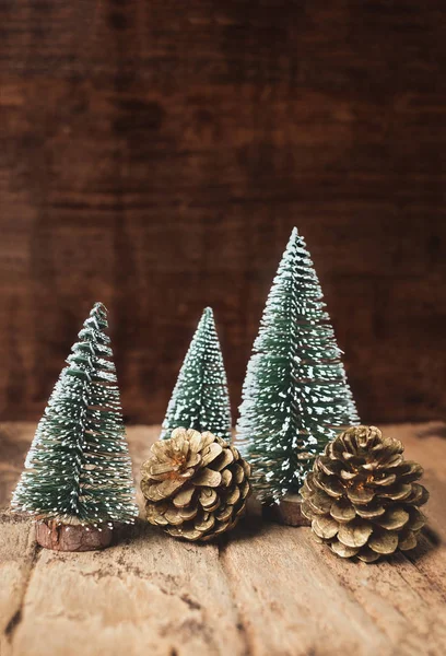 mini christmas tree and pine cone wood on rustic wooden table and dark brown hardwood wall.winter holiday seasonal greeting card.leave space to adding text or design