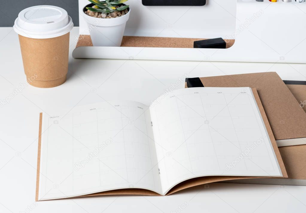 top view of open calendar planner with modern office stationery and take away coffee cup on white desk in office.mock up space of organizer table notebook