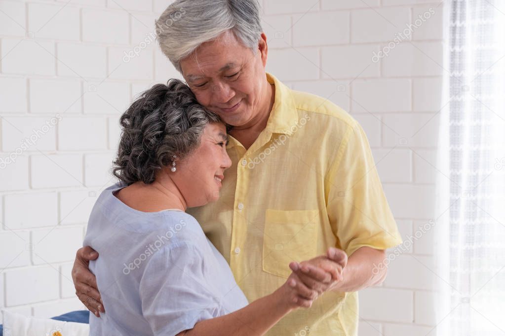 Happy Asian senior couple enjoy slow dancing at living room in house with warm love emotion.grandmother snuggle grandfather