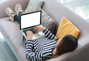 Asyalı kadın kanepede uzanmış ve alay boş ekranlı dizüstü bilgisayar kullanan ekran veya tasarım montaj, kırpma yolu üstünde perde, Modern dijital yaşam tarzı için rahat bez.