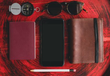 Cep, pasaport, defter, güneş gözlüğü, pusula ve rustik kırmızı ahşap yuvarlak masa pencere yakınındaki üzerinde beyaz kalem kümesi. Tropikal yaz tatili tatil concept.clipping yolda smartphone ekran