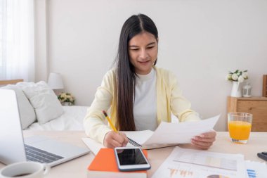 Asyalı kadın serbest meslek dizüstü ve Not evde yatak odasında masada aşağı zerre rapor okuma. Evde concept.work üzerinden home.relax yaşam tarzı çalışma