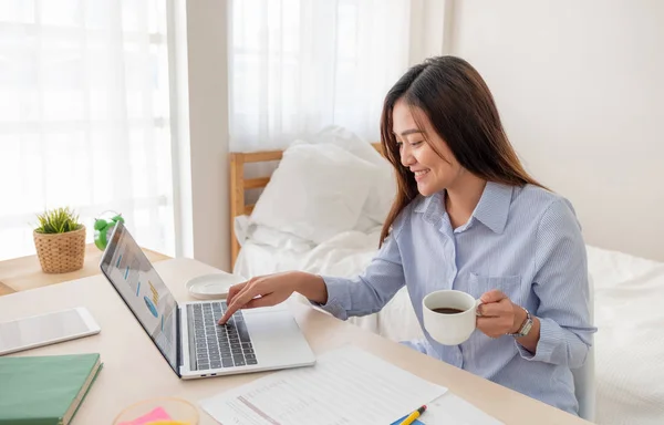 Asiatiska kvinnliga frilansare dricker kaffe och och arbetar på laptop en — Stockfoto