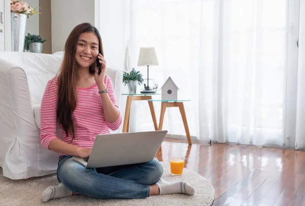 Felice donna asiatica parlare su cellulare e digitando computer portatile a — Foto Stock