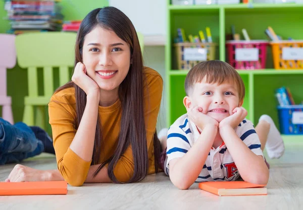 Niño y maestro mirando a la cámara y sonriendo acostado en la escuela — Foto de Stock