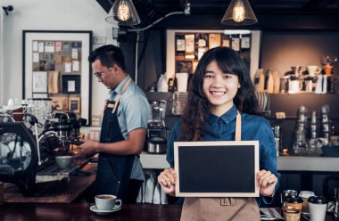 Asyalı kadın barista boş yazı tahtası co tutan jean önlük giymek