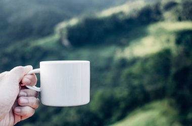 Yeşil blur dağ doğa ormanında sıcak kahve fincanı tutan el