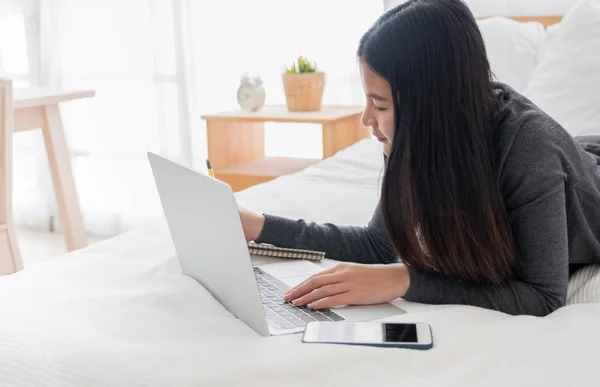 Asiatico donna posa su letto fare scartoffie su laptop in bedroom.w — Foto Stock