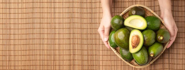 Hand holding organic avocados half cut with seed and whole fruit