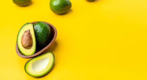 organic avocados half cut with seed and whole fruit in wood bowl