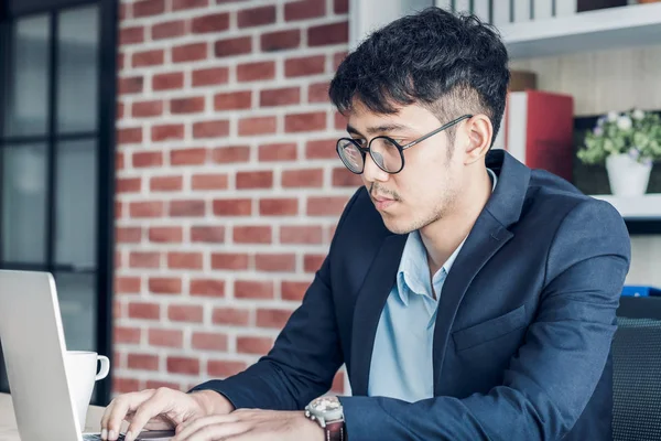 Молодой азиатский бизнесмен носит костюм, работая с ноутбуком на столе та — стоковое фото