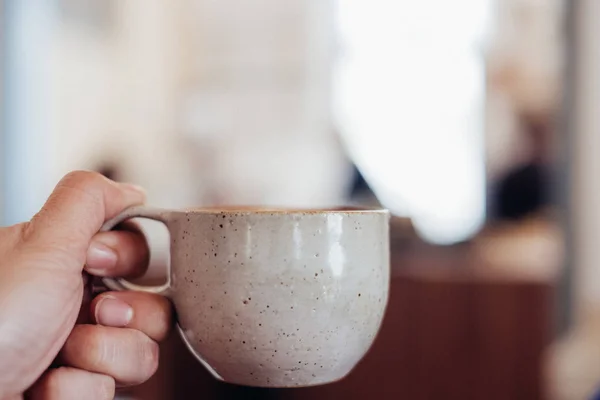 Z bliska ręka trzyma filiżankę gorącej filiżanki kawy cappuccino z — Zdjęcie stockowe