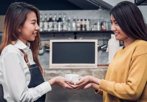 Ung asiatisk kvinna barista hålla kaffekopp betjäna en kund på th — Stockfoto