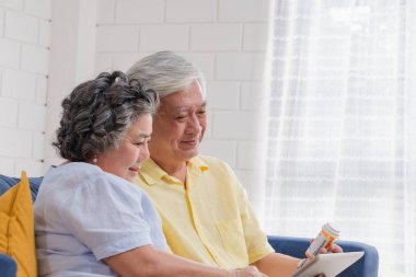 Asya kıdemli çift kullanım tablet video konferans hakkında evde kanepede otururken hap doktor ile üst düzey öğrenmek technology.aging evde kullanmak için