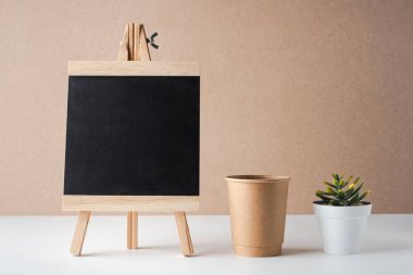 Kağıt bardaklı boş karatahta ve beyaz masadaki yeşil bitki.