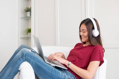 Kulaklıkla müzik dinleyen Asyalı bir kadın ve dizüstü bilgisayar kullanıyor.