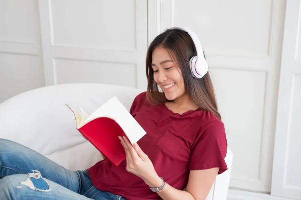 Asyalı kadın kulaklıkla müzik dinliyor ve R ile kitap okuyor. — Stok fotoğraf