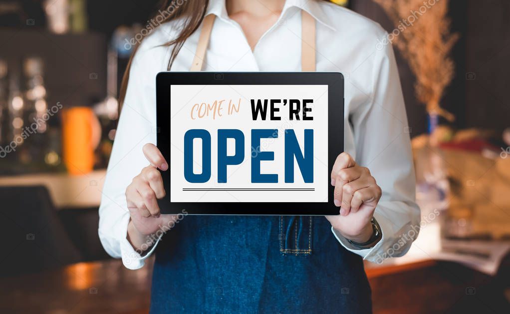 woman barista wear jean apron holding come in we are open sign o