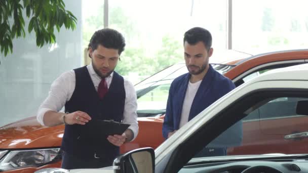 Distribuidor de coches profesional que vende nuevo auto a un hombre joven — Vídeo de stock