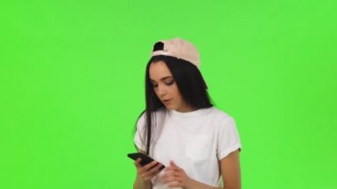 Yeşil arka plan üzerinde onun akıllı telefon kullanan muhteşem genç kadın. Chromakey üzerinde poz gülümseyerek, ona telefon ile selfies alarak çekici neşeli bir kadın. Teknoloji, sosyal medya, bağlantı.