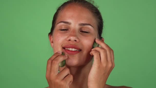 Piękna kobieta masuje jej twarz plasterkami ogórka — Wideo stockowe