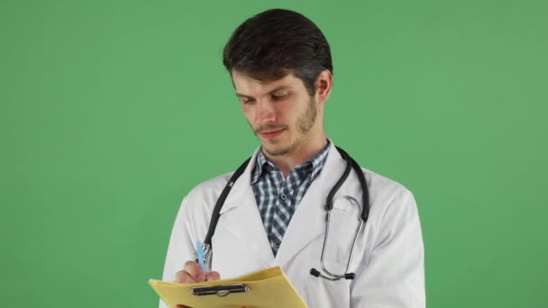 Junger Arzt schreibt auf Klemmbrett auf grünem Chromakey — Stockvideo