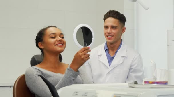 Красива жінка перевіряє свою посмішку у дзеркалі в стоматологічній клініці — стокове відео
