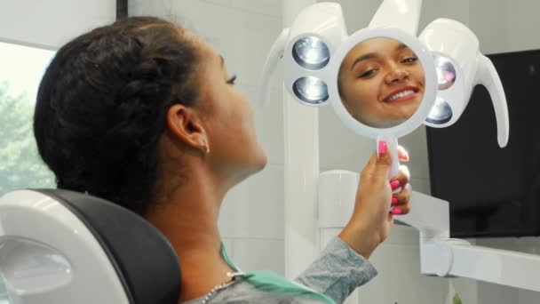 Веселая африканская женщина улыбается, рассматривая свою здоровую улыбку в зеркале — стоковое видео