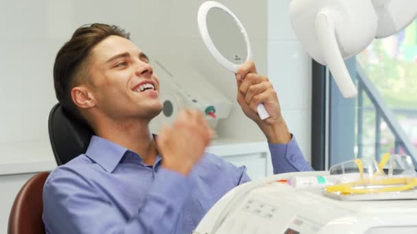 英俊的年轻人检查他的牙齿在镜子在牙科诊所 — 图库视频影像
