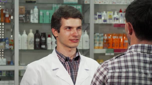 Мужчина-фармацевт разговаривает со своим клиентом в аптеке — стоковое видео