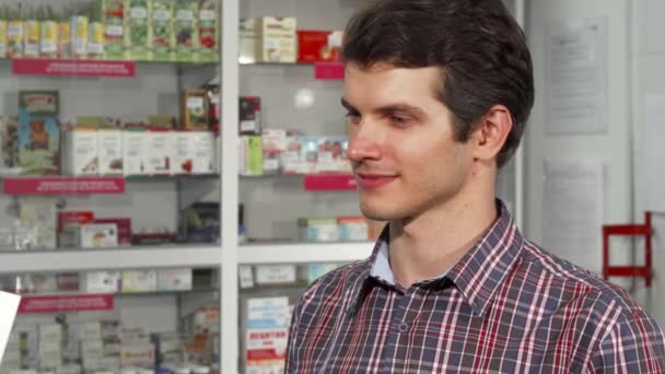 Feliz hombre guapo sonriendo sosteniendo bolsa de compras en la farmacia — Vídeos de Stock