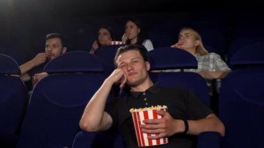Yakışıklı delikanlı arıyorum sıkılmış ve sinemada otururken yorgun. Çekici erkek seyirci sinemada uykuya dalmak. Film izlerken yorgun bir adam. Eğlence, yaşam kavramı.