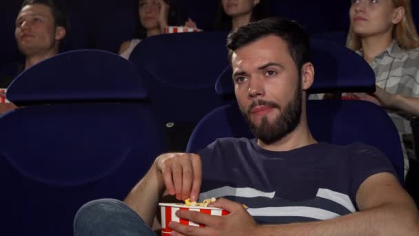 Attraente giovane uomo mangiare popcorn durante il film noioso al cinema — Video Stock