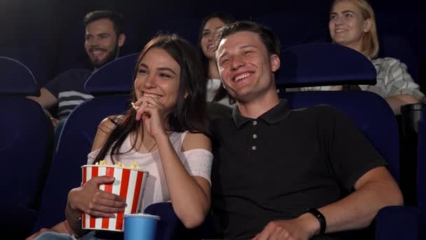 Счастливая пара смеётся во время просмотра комедийного фильма в кинотеатре — стоковое видео