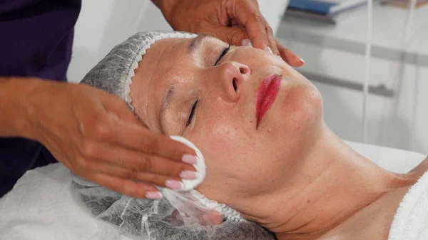 Güzellik uzmanı yüzünü Pamuklu ped ile temizlik sırasında gülümseyen kadın kıdemli