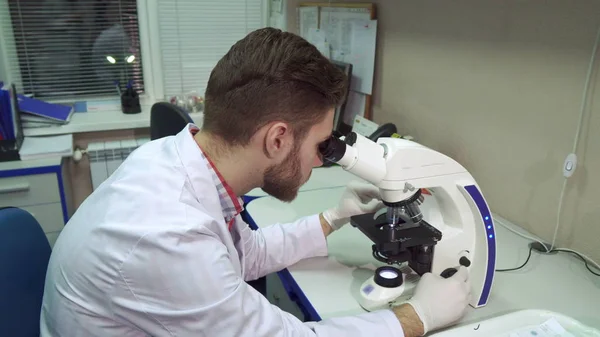 Man moves stage clipse on microscope at the laboratory