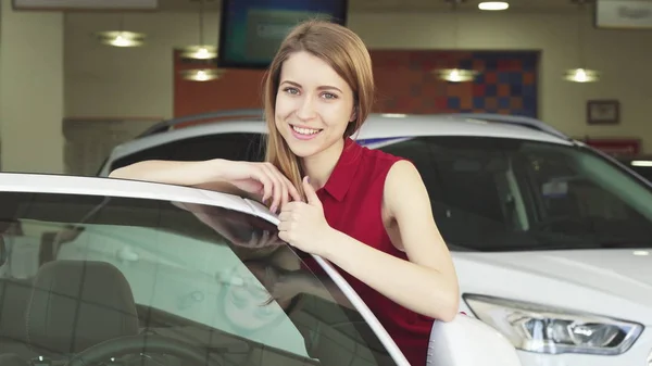 Schöne junge Frau posiert mit einem neuen Auto im Autohaus — Stockfoto