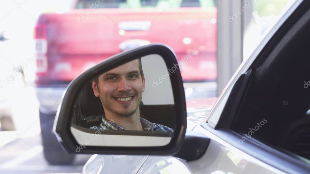 Close up of a side mirror of a car, happy male driver smiling