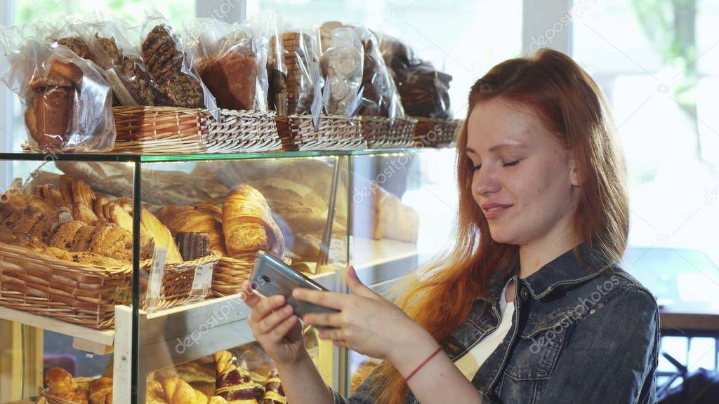 Cheerful woman taking photos of pastry at the bakery store